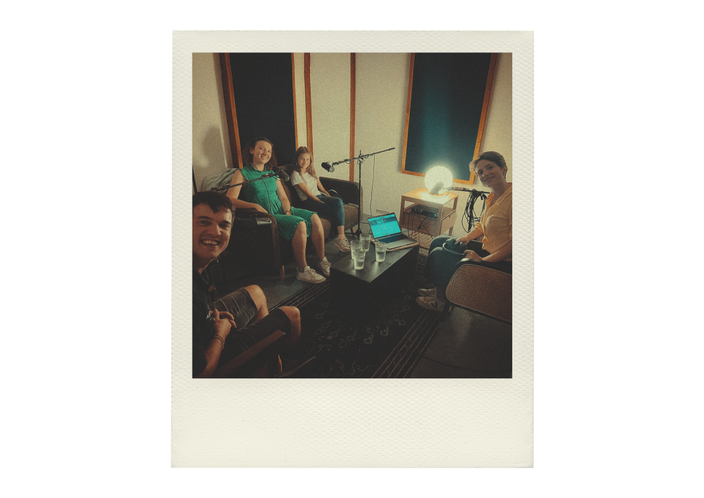 Auf dem Bild ist ein Studio zu sehen. Um einen schwarzen Couchtisch herum sitzen Sebastian, VHS-Lehrerin Magda, Schülerin Tizi und Katharina (von links nach rechts). Auf dem Couchtisch stehen vier Gläser Wasser und ein Laptop. Dahinter steht eine runde Lampe.