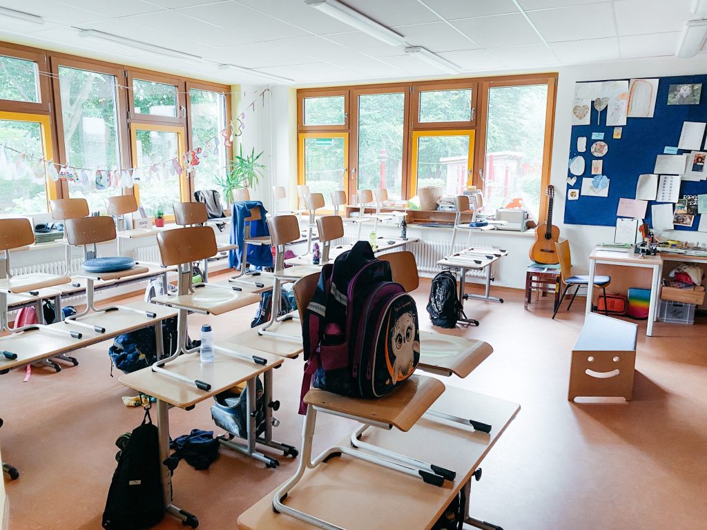 Klassenzimmer, mehrere Tische und eine bunte schultasche im Vordergrund