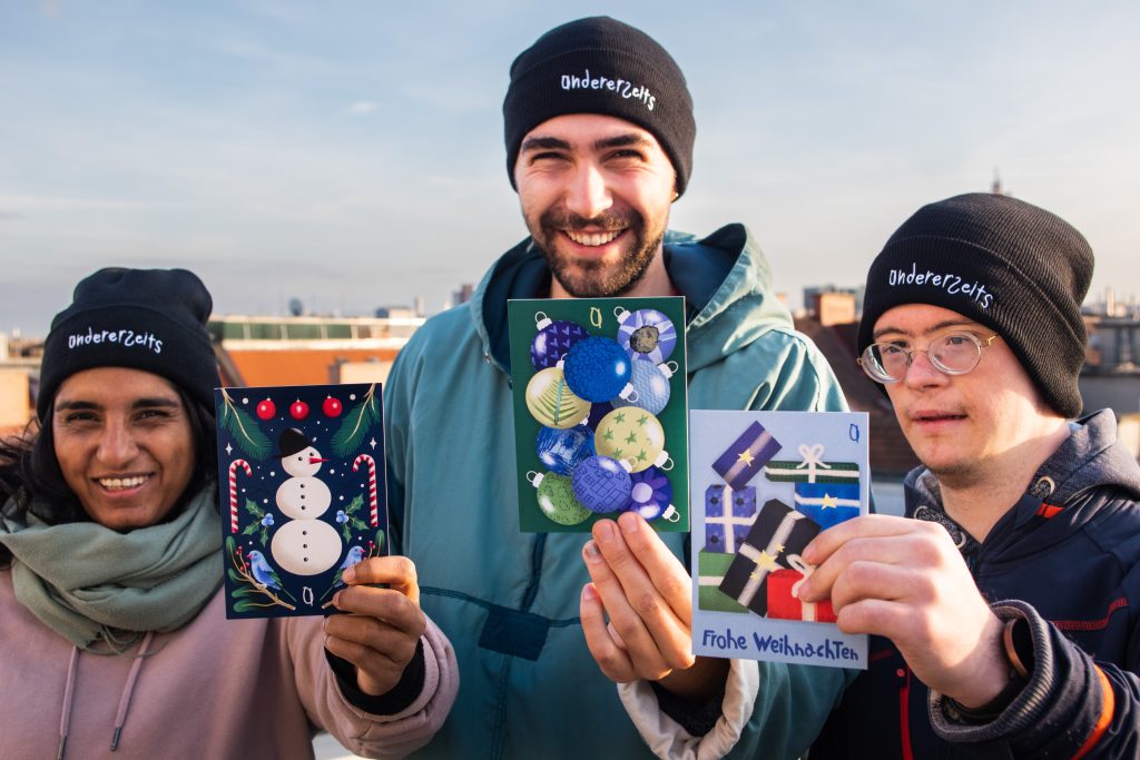 Drei junge Menschen, die andererseits Postkarten in die Kamera halten.