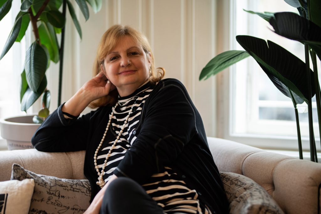 Petra Smutny sitzt in einem Stuhl. Sie stütz das Gesicht mit der linken Hand. Sie hat blonde Haare und schaut in die Kamera.