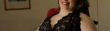 Leonie Schüler sitzt in ihrem Rollstuhl. Sie lächelt und schaut nach oben. Sie trägt einen schwarzen Spitzen-Body und pinken Lippenstift.