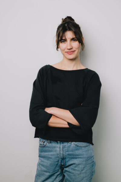 Foto von Ramona. Sie trägt ein schwarzes Oberteil und hat ihre Haare zu einem Dutt gebunden