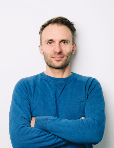Ein weisser Mann mit kurzen Haaren blickt in die Kamera. Er trägt einen blauen Pullover.