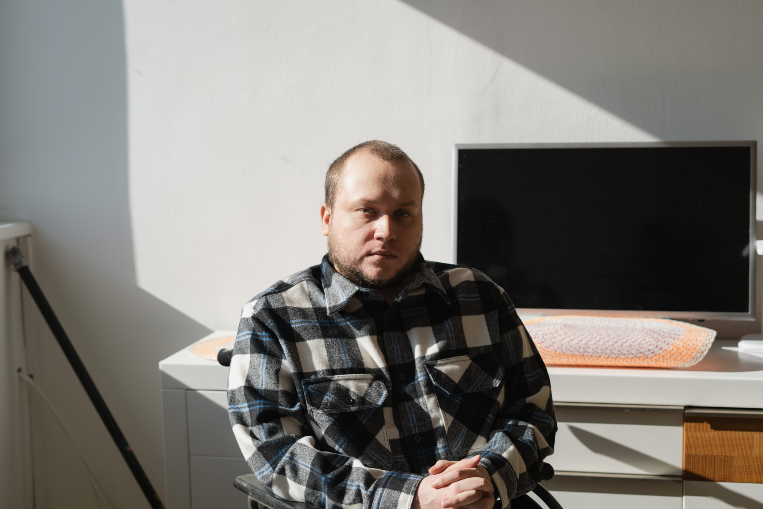 Anton schaut mit ernstem Blick in die Kamera. Er hat kurze, braune Haare und trägt ein Karo-Hemd. Hinter ihm steht ein Computer-Bildschirm auf einem Schreibtisch.