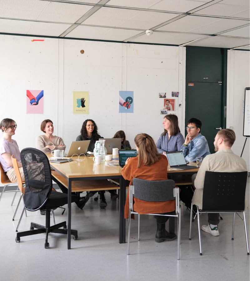 Menschen mit und ohne Behinderungen sitzen um einen Tisch und arbeiten miteinander