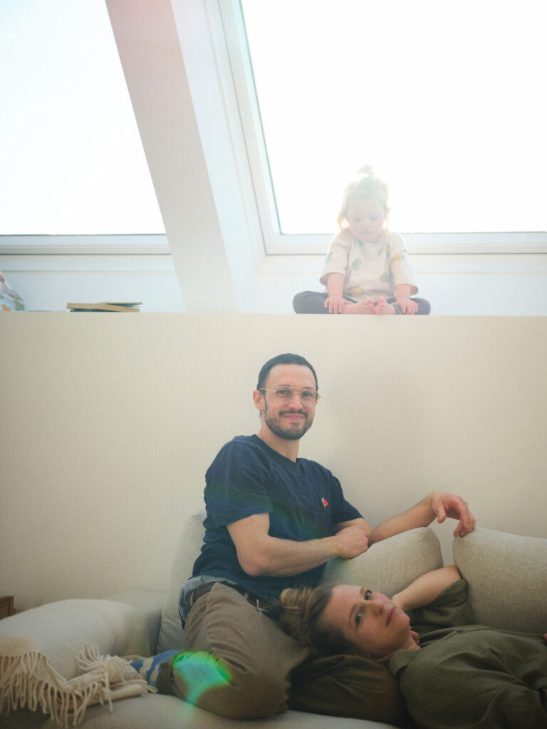 Lukas sitzt auf der Couch und Valerie liegt mit dem Kopf auf ihn gestützt. Sie schauen freundlich in die Kamera. Darüber sitzt Emil auf einer hohen Fensterbank und schaut auf die beiden herab.