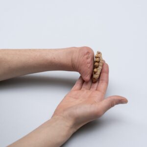 Eine Person hält eine Kurkuma-Knolle in der offenen Hand. Die andere Hand ist individuell geformt. Die Wurzel sieht aus wie kleine Finger.