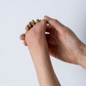 Eine Hand hält ein Stück einer Kurkuma-Knolle fest. Die Wurzel hat viele kleine Knoten und erinnern an kleine Finger.