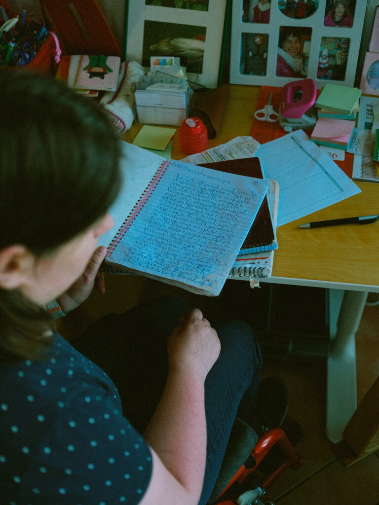 Das Foto zeigt ein offenes Tagebuch, das auf einem Schreibtisch liegt. In der linken Ecke sitzt eine junge Frau.