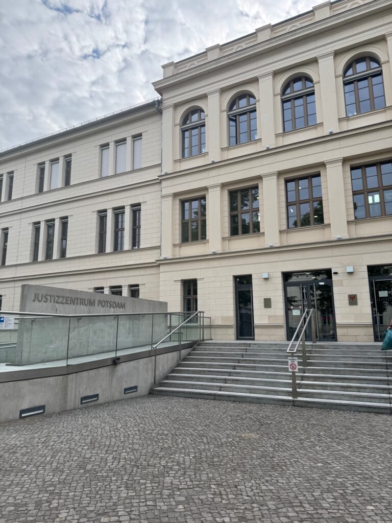 Das Foto zeigt den Eingang des Justizzentrum Potsdam. Ein zweistöckiges Gebäude. Zu dem Eingang führt eine Stiege hinauf.