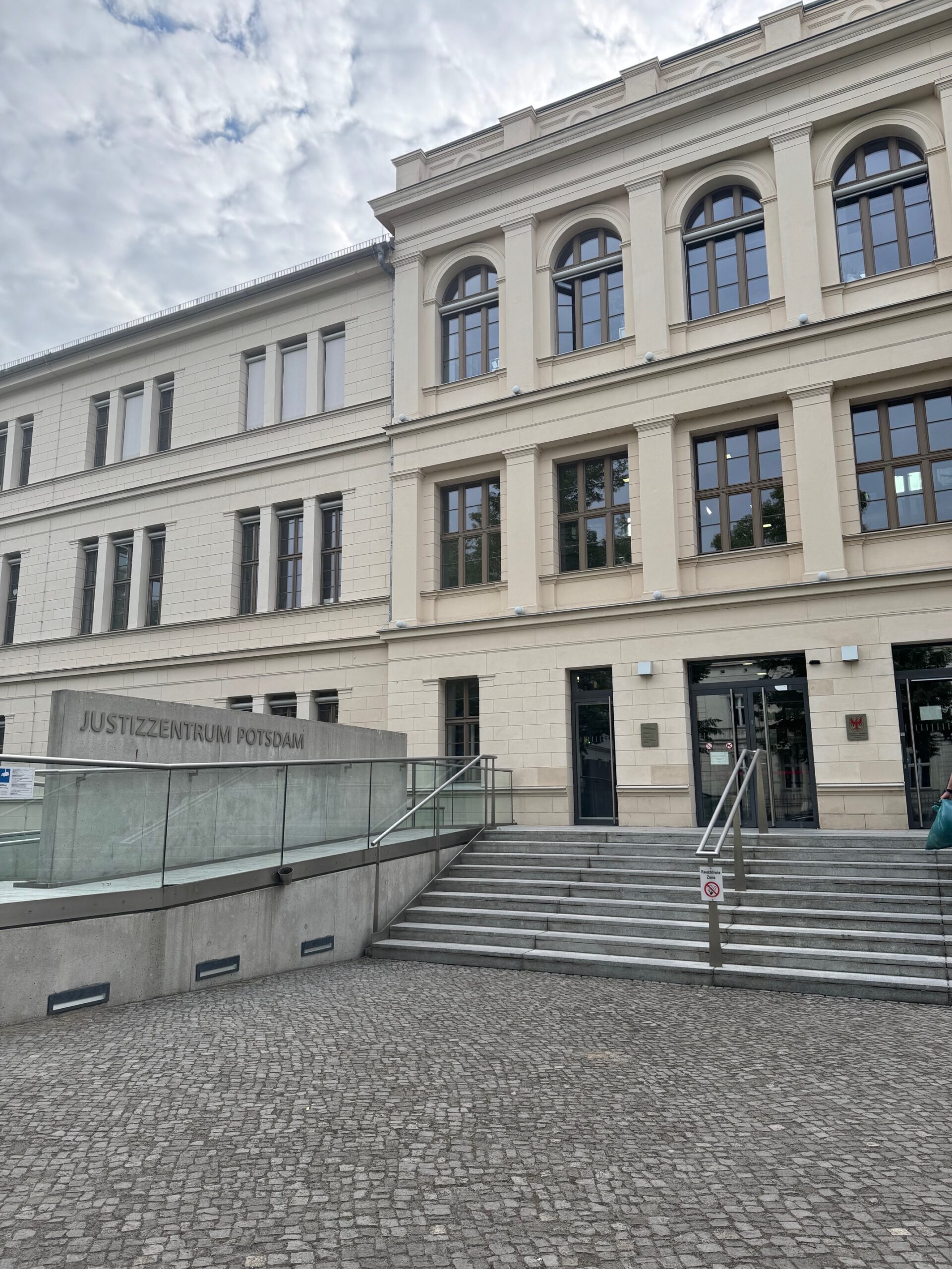Das Foto zeigt den Eingang des Justizzentrum Potsdam. Ein zweistöckiges Gebäude. Zu dem Eingang führt eine Stiege hinauf.