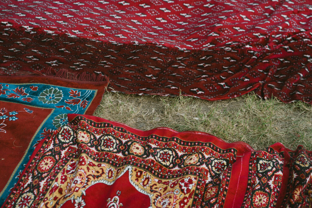 Mehrere bunte Teppiche liegen auf Gras. Man sieht rote, braune und blaue Muster.