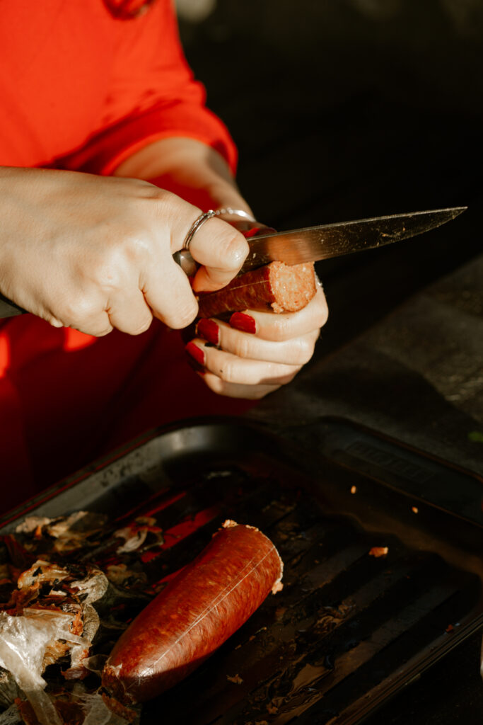 Eine Person schneidet mit dem Messer in eine Wurst.