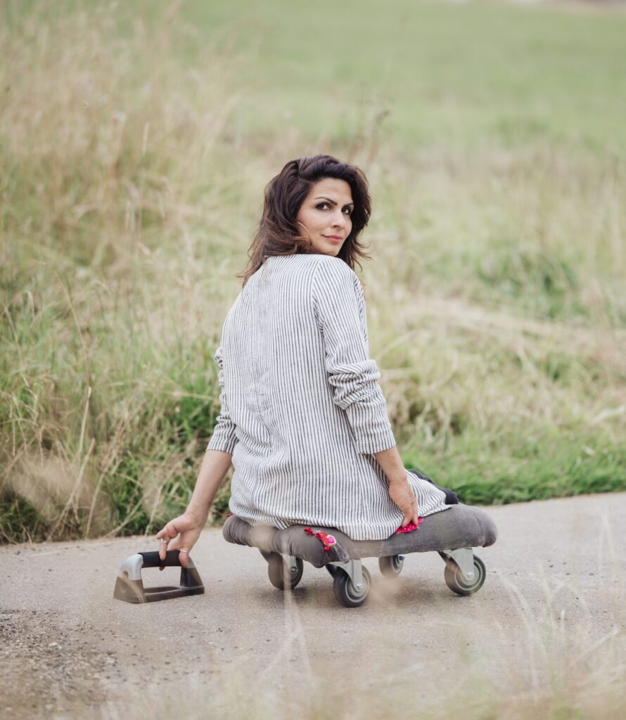 Hülya Marquard sitzt auf einem Skate-Board. Sie schaut mit freundlichen Blick über die Schulter. Sie ist im Grünen.