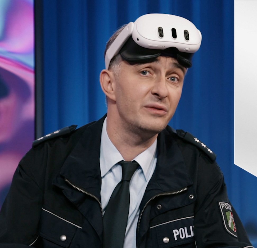 Das Bild zeigt Jan Böhmermann, einen bekannten Moderator, der hinter einem Tisch sitzt. Er trägt einen Polizeiuniform. Rechts neben ihm sieht man eine Grafik mit der Aufschrift „andererseits – Magazin für Behinderung und Gesellschaft“. Der Hintergrund ist bunt und modern gestaltet.