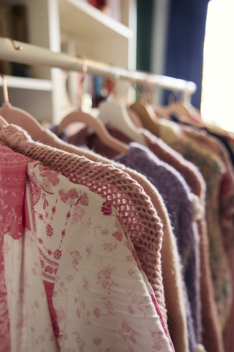 Auf einer Kleiderstange hängen mehrere Oberteile. Viele von ihnen sind Strick-Oberteile. Sie haben bunte Farben.