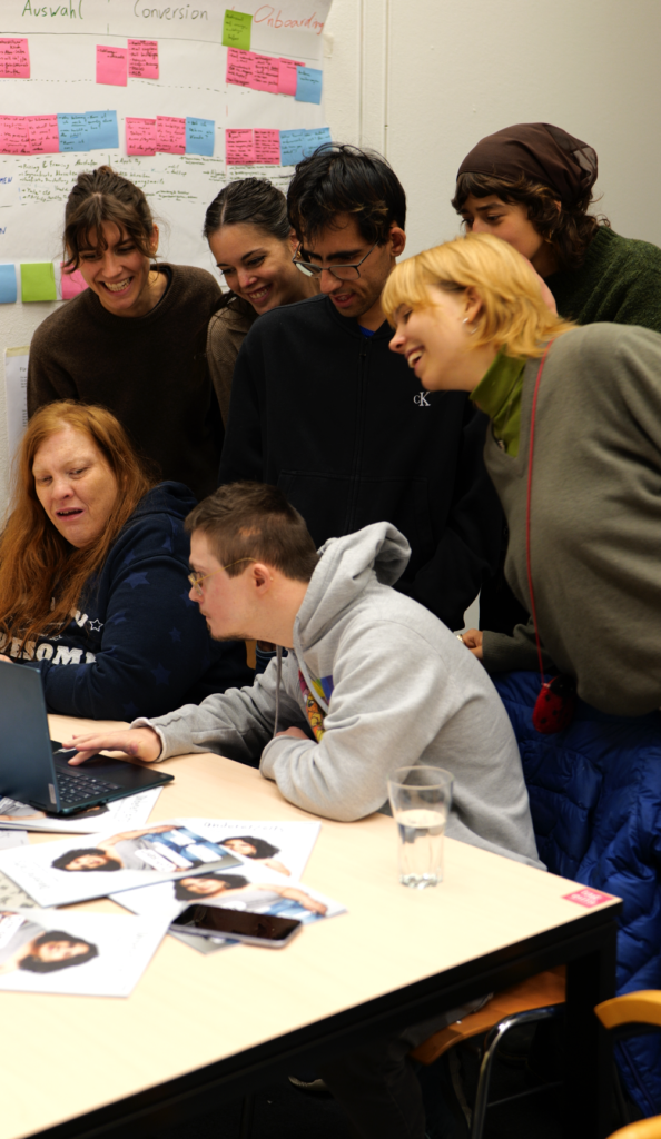Menschen mit und ohne Behinderungen schauen gemeinsam in einen Laptop und lachen