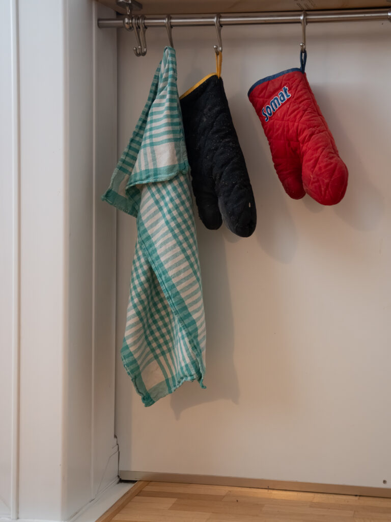 Auf einer Metallstange hängt ein Geschirrtuch und zwei Hitzehandschuhe nach unten.