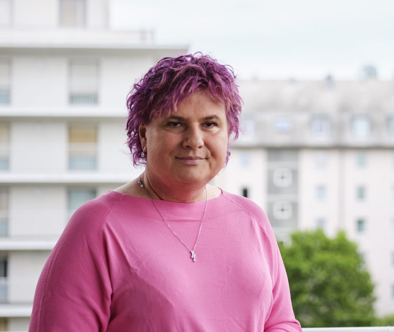 Eine Person schaut mit ernstem Blick in die Kamera. Sie hat kurze pinke Haare und trägt ein pinkes Shirt.