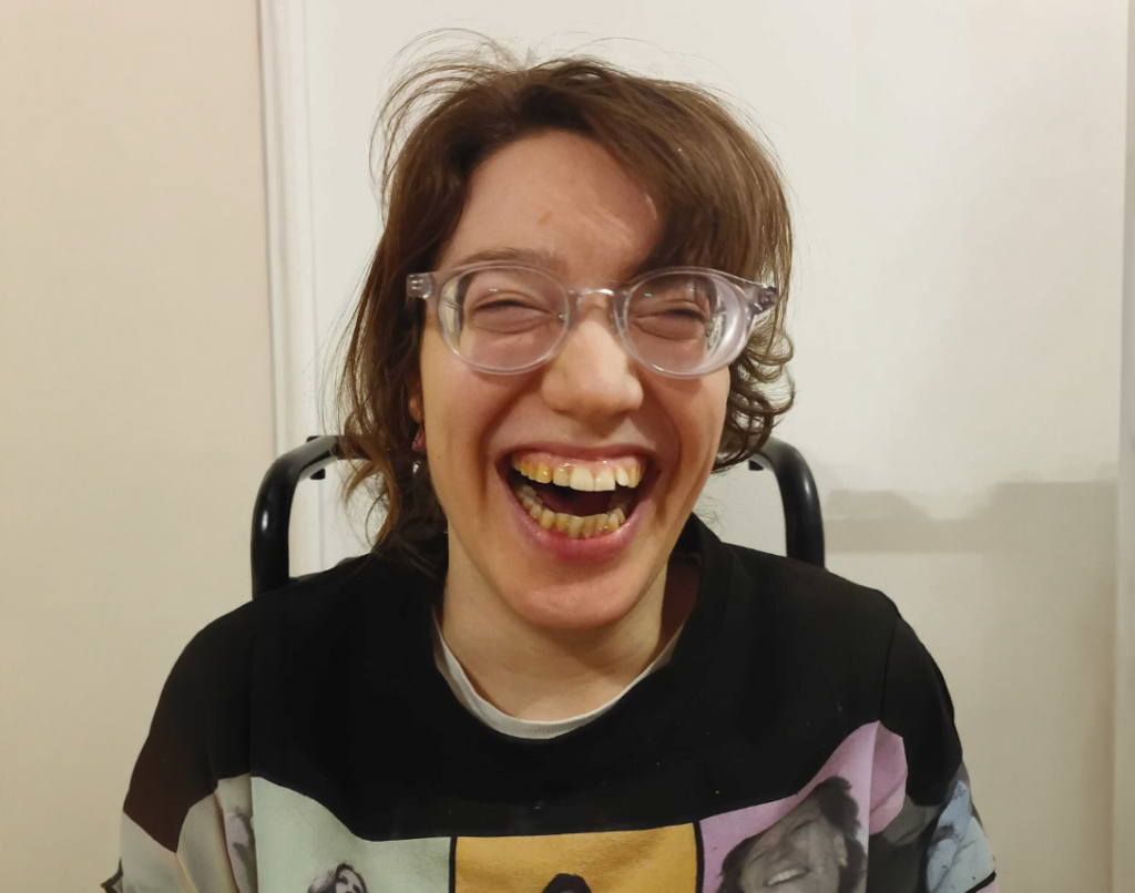 Eine Frau schaut lachend in die Kamera. Sie trögt eine Brille und hat kurze braune Haare.