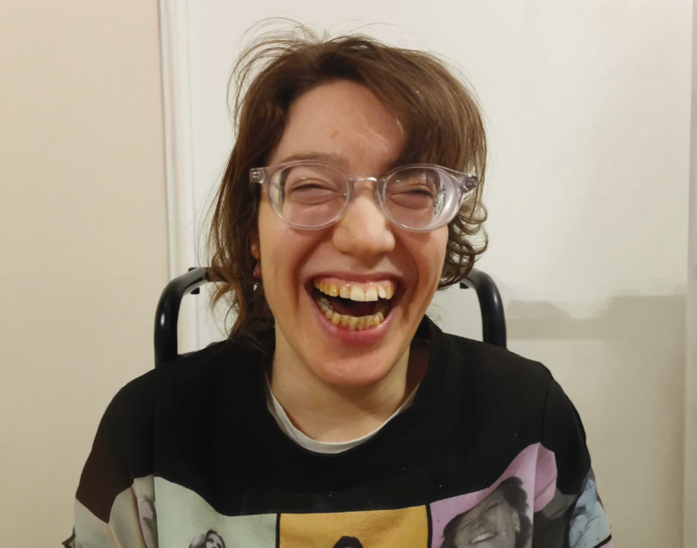 Eine Frau schaut lachend in die Kamera. Sie trögt eine Brille und hat kurze braune Haare.