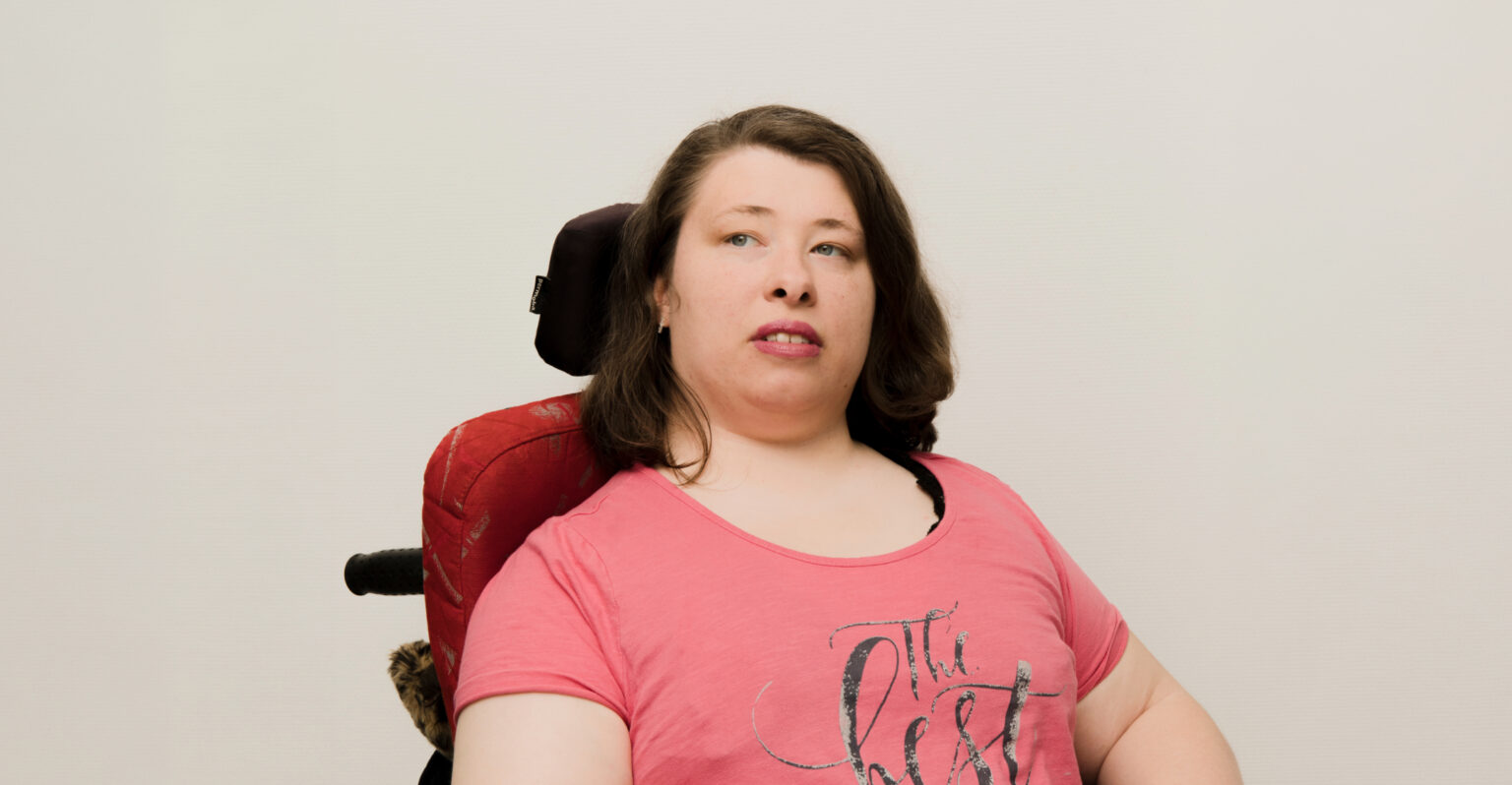 Eine Frau schaut mit ernsten Blick nach links. Sie trägt ein rotes T-Shirt und einen roten Lippenstift.