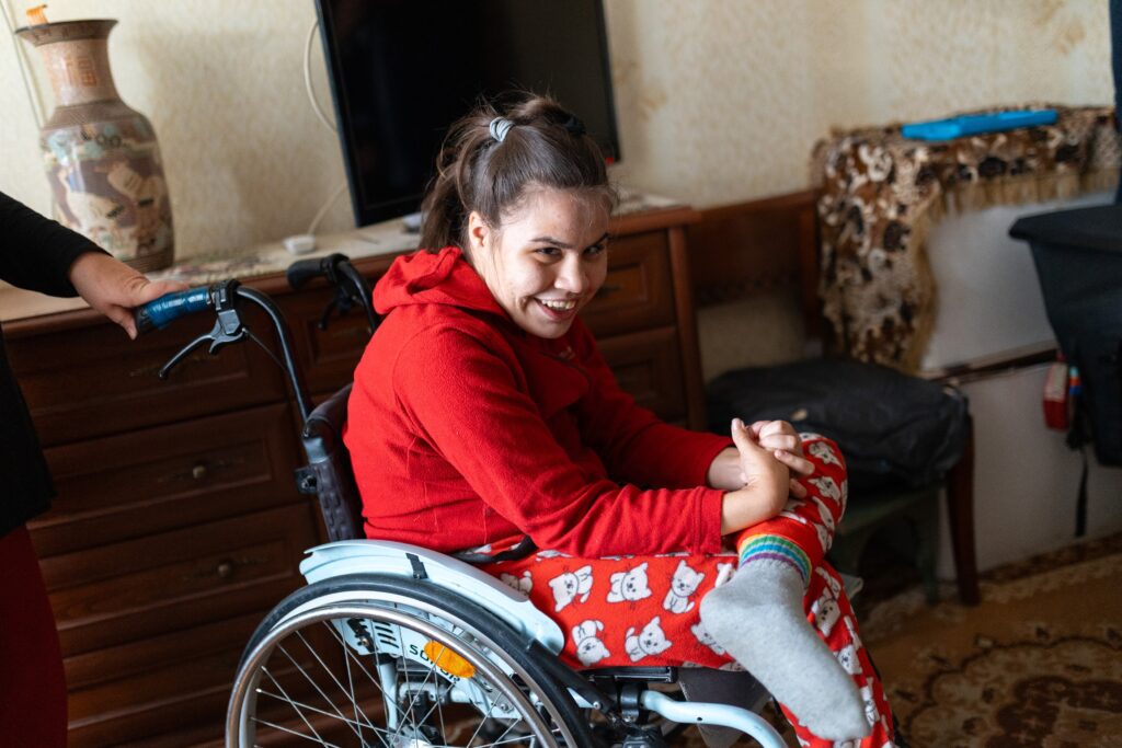 Eine junge Frau schaut mit freundlichen Blick nach rechts. Sie benutzt einen Rollstuhl.