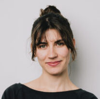 Eine Frau mit braunen, hochgebundenen Haaren schaut mit freundlichen Blick in die Kamera.