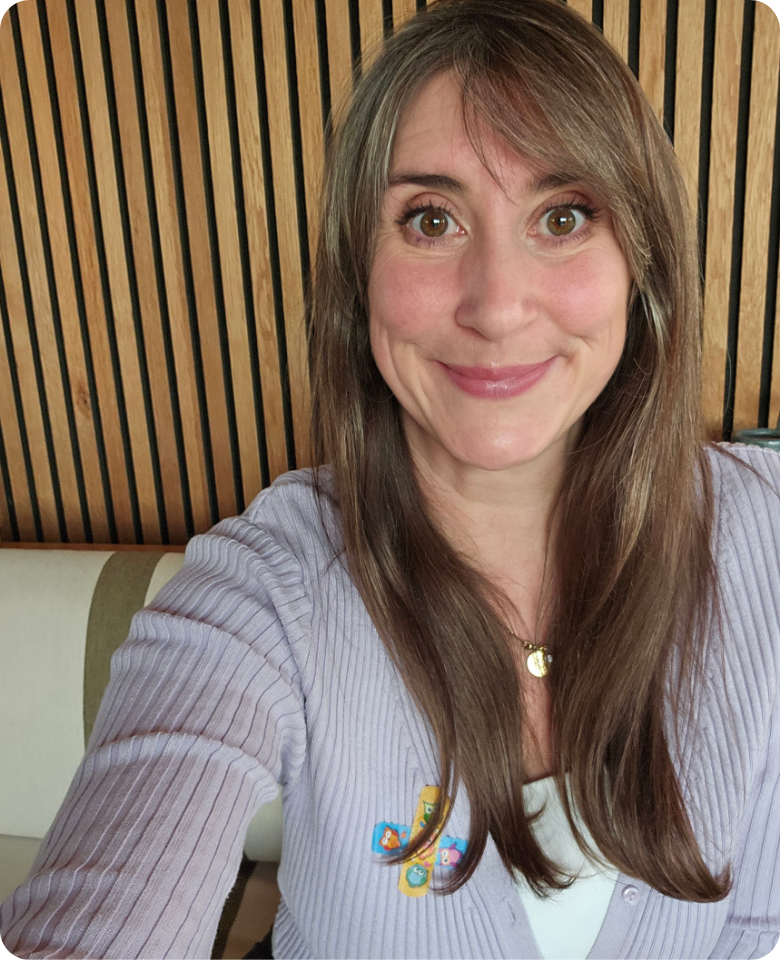 Eine Frau lächelt in die Kamera. Sie hat lange braune Haare und trägt eine graue Bluse.