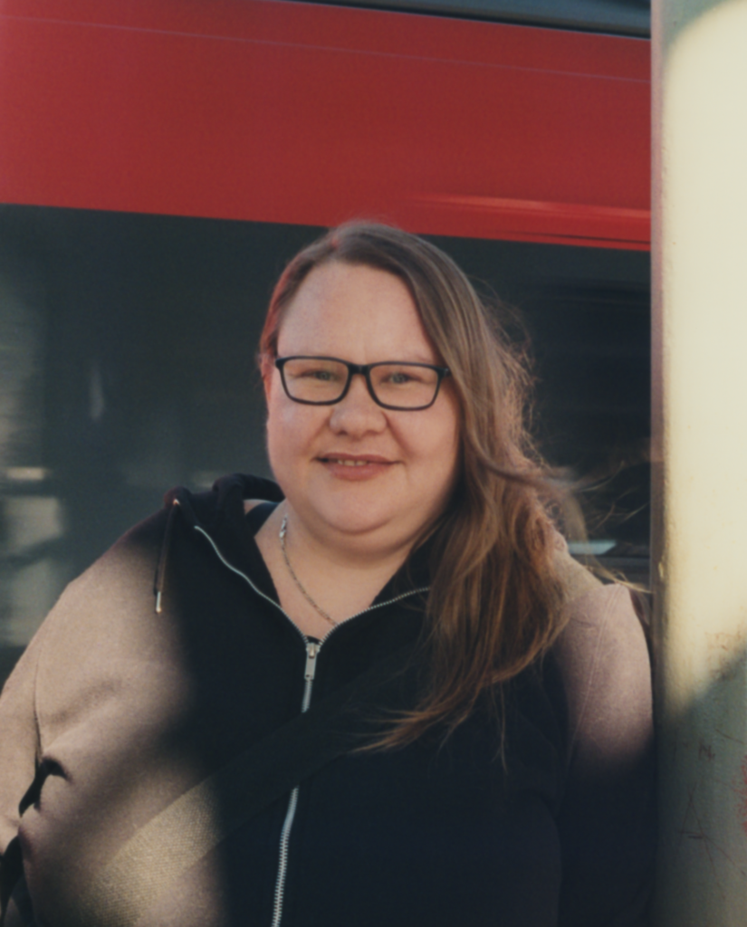 Eine Frau scaut mit freundlichen Blick in die Kamera. Sie hat lange dunkelblonde Haare und trägt eine Brille.