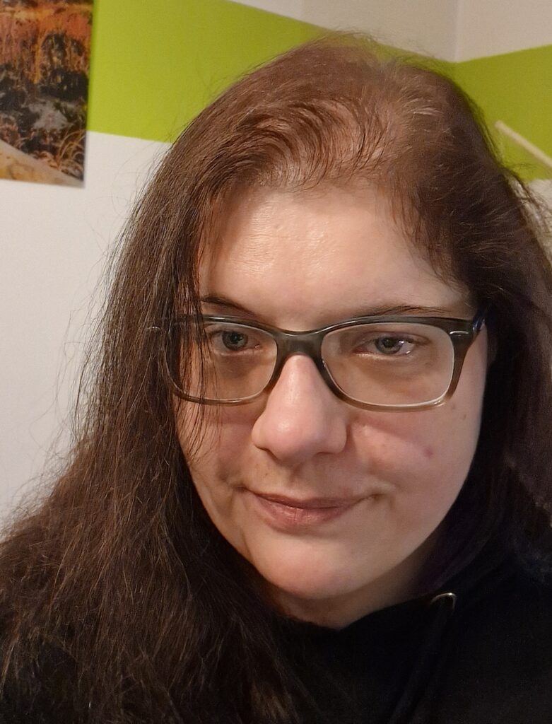 Eine Frau schaut mit ernstem Blick in die Kamera. Sie hat dunkelbraune Haare und trägt eine Brille.