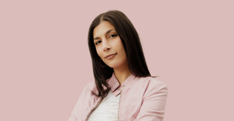 Eine junge Frau schaut mit leichten freundlichen Blick in die Kamera. Sie hat dunkelbraune glatte Haare und dunkelbraune Augen. Sie trägt eine rosa Jacke. Der Hintergrund ist ebenso rosa.