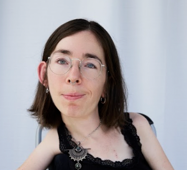 Der Ausschnitt zeigt eine junge Frau. Sie hat dunkle Haare und eine Brille. Sie schaut. mit freundlichen Blick in die Kamera.